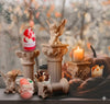 Decorative candles in glass cups displayed with angel figurines and autumn decor